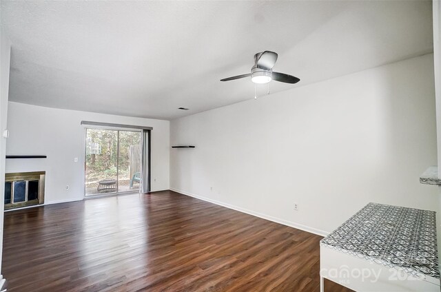 unfurnished living room featuring dark wood finished floors, a glass covered fireplace, a ceiling fan, and baseboards