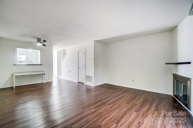 unfurnished living room with a glass covered fireplace, dark wood-type flooring, a ceiling fan, and baseboards