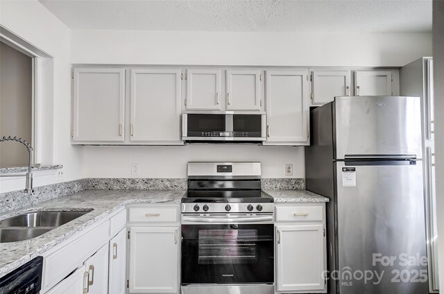 kitchen with stainless steel appliances, a sink, light stone counters, a textured ceiling, and white cabinetry