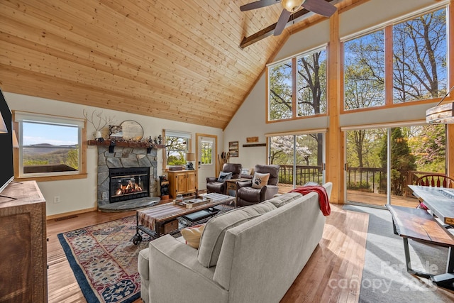 living area with high vaulted ceiling, a ceiling fan, a stone fireplace, and a wealth of natural light