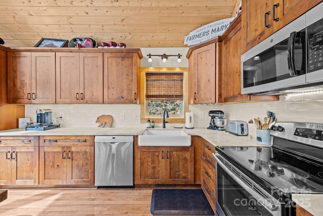 kitchen featuring brown cabinets, a sink, light countertops, light wood-style floors, and stainless steel appliances