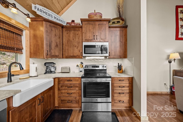 kitchen with lofted ceiling, wood finished floors, light countertops, a sink, and stainless steel appliances