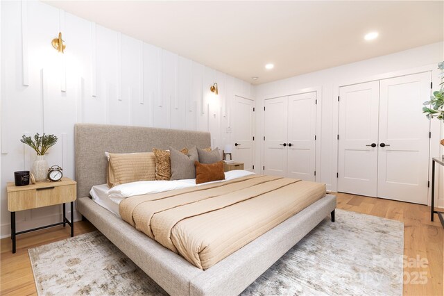 bedroom with recessed lighting, two closets, and light wood-style floors