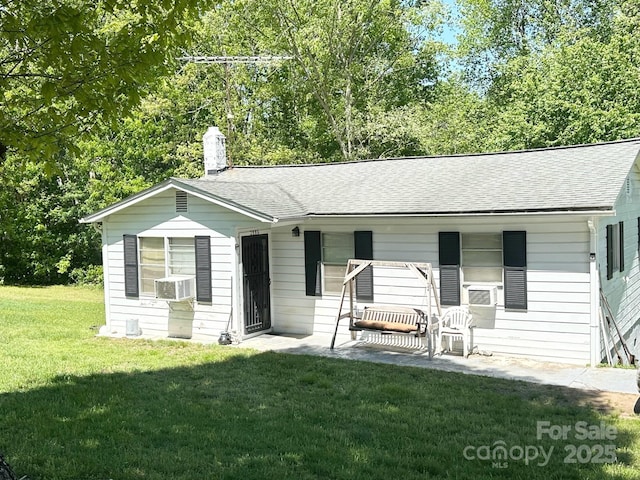 ranch-style house with a chimney, roof with shingles, cooling unit, a front lawn, and a patio
