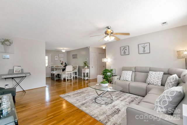 living room featuring visible vents, baseboards, ceiling fan, and light wood-type flooring