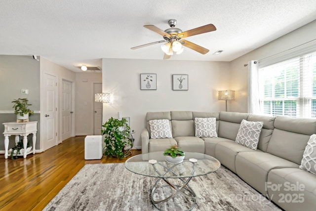 living area with ceiling fan, a textured ceiling, visible vents, wood finished floors, and baseboards