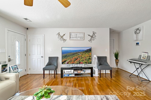 living room with wood finished floors, a ceiling fan, a textured ceiling, and visible vents