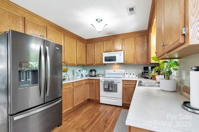 kitchen featuring a sink, light wood finished floors, white appliances, light countertops, and visible vents