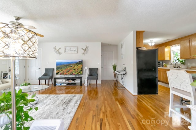 living room with a textured ceiling, ceiling fan, and light wood-style flooring