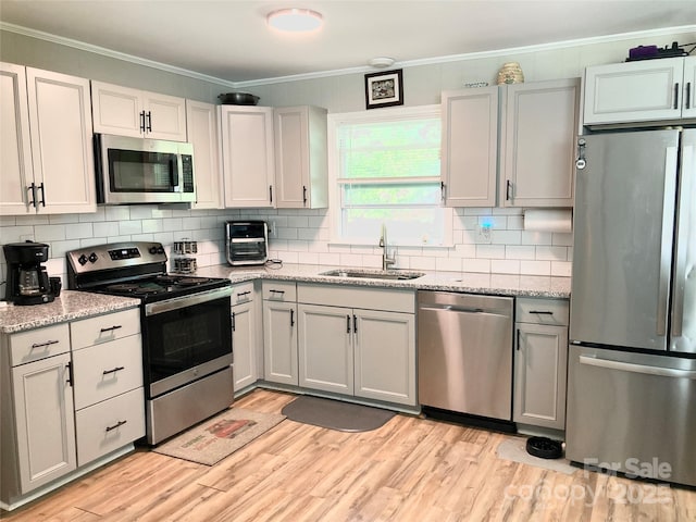 kitchen with a sink, light wood-style flooring, stainless steel appliances, tasteful backsplash, and ornamental molding