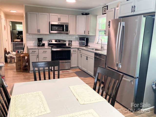 kitchen featuring appliances with stainless steel finishes, a sink, light wood-style floors, tasteful backsplash, and ornamental molding