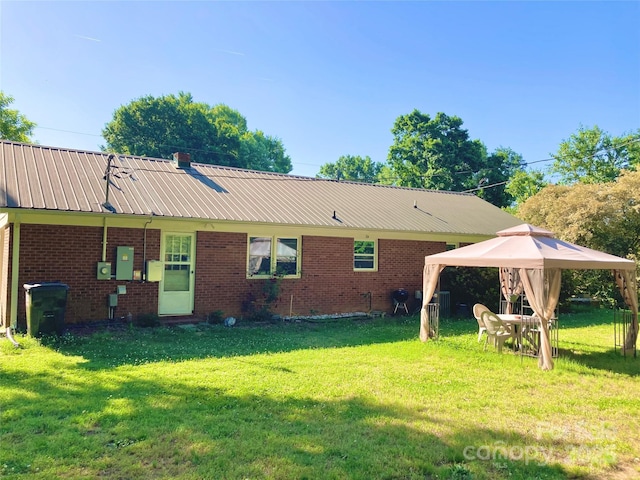 rear view of property with a lawn, a gazebo, and brick siding