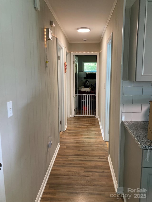 hallway featuring baseboards, ornamental molding, wooden walls, and dark wood-style floors