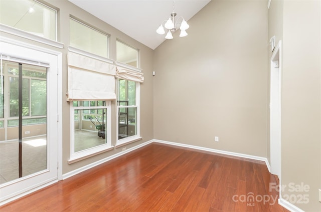 empty room with a chandelier, wood finished floors, healthy amount of natural light, baseboards, and high vaulted ceiling
