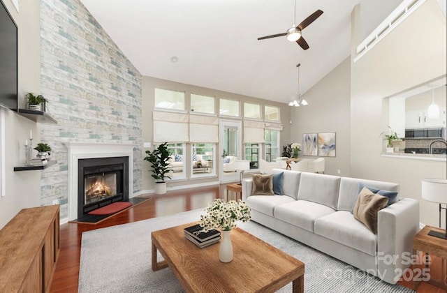 living area featuring high vaulted ceiling, wood finished floors, ceiling fan, and a fireplace