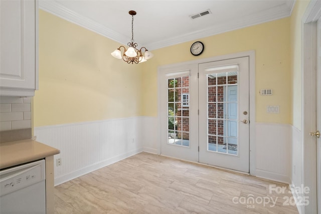 unfurnished dining area featuring french doors, ornamental molding, visible vents, a chandelier, and wainscoting