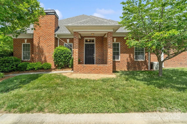 view of front facade with a shingled roof, a front lawn, a chimney, and brick siding