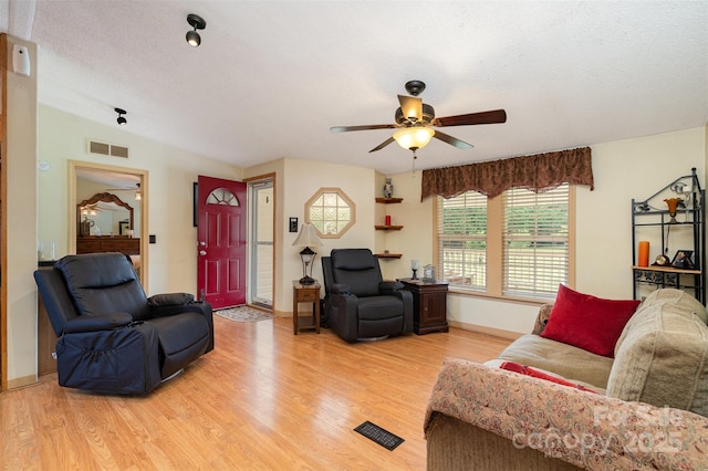 living room with a ceiling fan, light wood-style floors, visible vents, and a textured ceiling