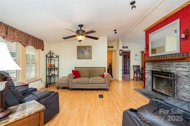 living area with a ceiling fan, a fireplace, lofted ceiling, and light wood-type flooring