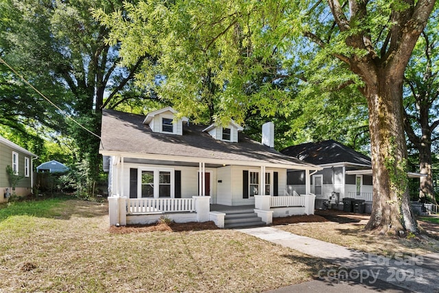 cape cod home featuring covered porch, a shingled roof, a chimney, and a front lawn