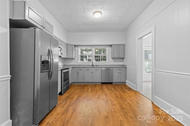 kitchen featuring a textured ceiling, light wood-type flooring, appliances with stainless steel finishes, and gray cabinetry
