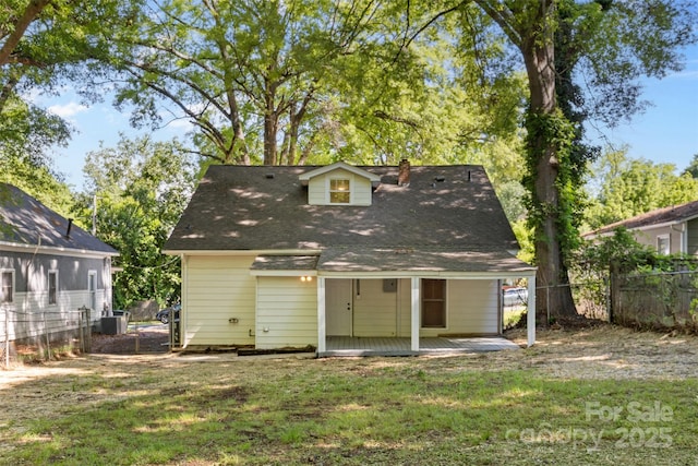 rear view of house with covered porch, cooling unit, a chimney, fence, and a lawn