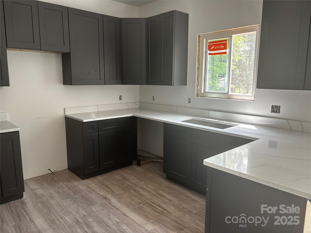 kitchen with light stone countertops, a sink, and light wood-type flooring