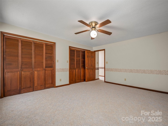 unfurnished bedroom featuring carpet floors, a ceiling fan, baseboards, and two closets