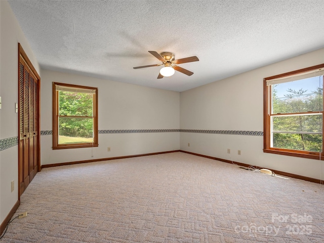 carpeted empty room with baseboards, ceiling fan, and a textured ceiling