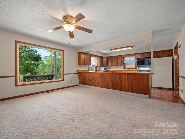 kitchen featuring light carpet, white appliances, a textured ceiling, brown cabinetry, and a peninsula