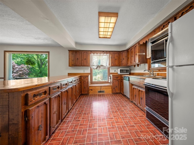 kitchen with brown cabinetry, a peninsula, brick patterned floor, white appliances, and light countertops