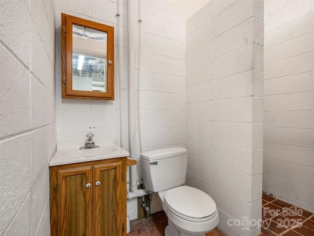 bathroom featuring toilet, concrete block wall, and vanity