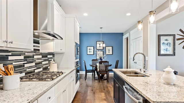 kitchen with a sink, dark wood finished floors, wall chimney exhaust hood, stainless steel appliances, and tasteful backsplash