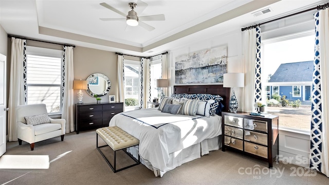 carpeted bedroom with visible vents, a raised ceiling, and ceiling fan