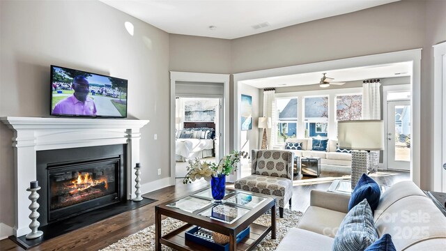 living room featuring dark wood-style flooring, a ceiling fan, a fireplace with flush hearth, and visible vents