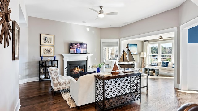 living room featuring a glass covered fireplace, baseboards, a ceiling fan, and dark wood-style floors