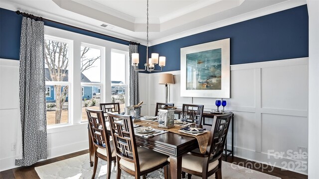 dining space featuring visible vents, a decorative wall, a wainscoted wall, a tray ceiling, and a chandelier