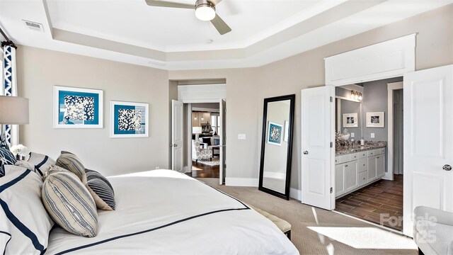 carpeted bedroom with a raised ceiling, ensuite bathroom, a ceiling fan, and visible vents