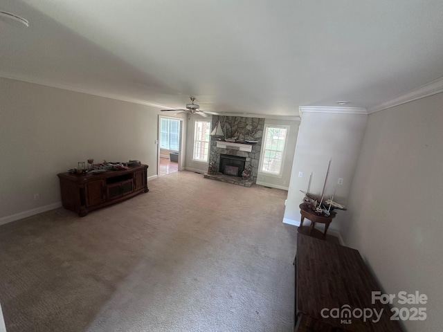 carpeted living room featuring baseboards, ornamental molding, a ceiling fan, and a stone fireplace