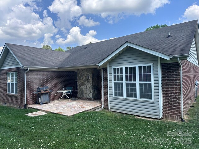 rear view of property featuring a patio, a shingled roof, a yard, and brick siding