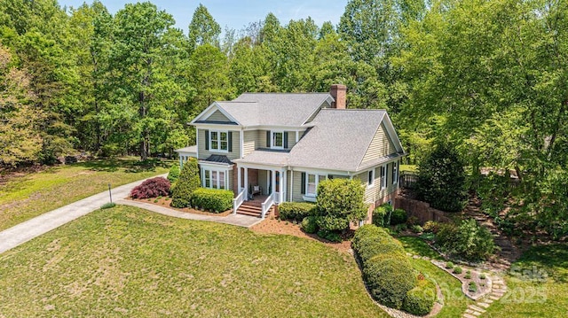 traditional-style house featuring roof with shingles, a chimney, a porch, and a front lawn