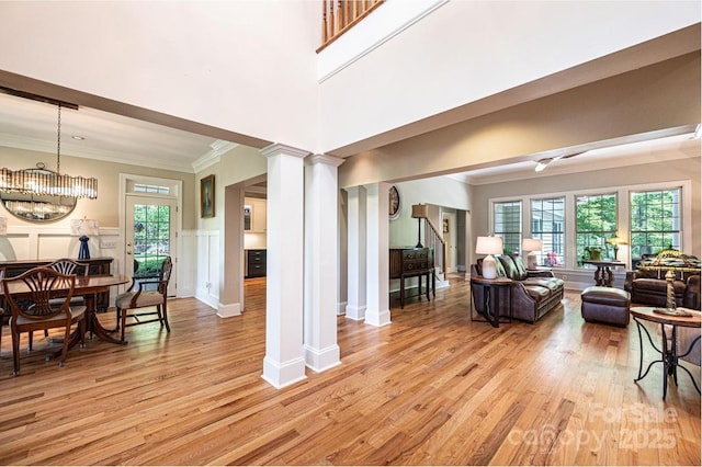 living area featuring light wood-style floors, ornamental molding, decorative columns, and plenty of natural light