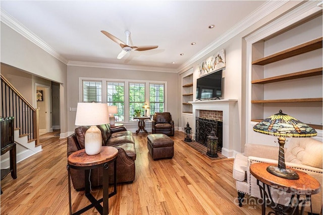 living room featuring ornamental molding, light wood-style flooring, ceiling fan, and stairway