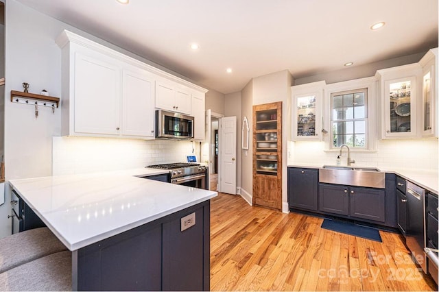 kitchen with appliances with stainless steel finishes, tasteful backsplash, light wood-type flooring, a sink, and white cabinetry