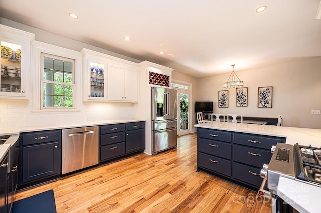 kitchen with appliances with stainless steel finishes, light wood-type flooring, light countertops, an inviting chandelier, and white cabinetry