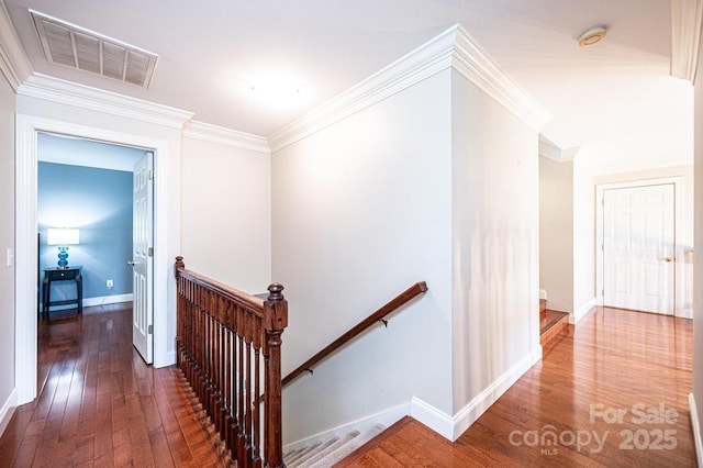 hall with crown molding, hardwood / wood-style flooring, an upstairs landing, and visible vents