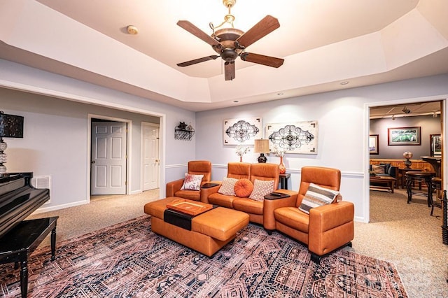 living area with a tray ceiling, a wood stove, carpet, and a ceiling fan