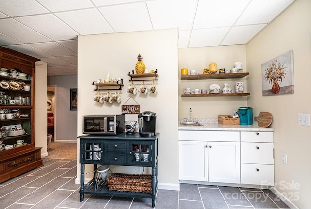 bar with a sink, indoor wet bar, stainless steel microwave, a drop ceiling, and dark tile patterned flooring