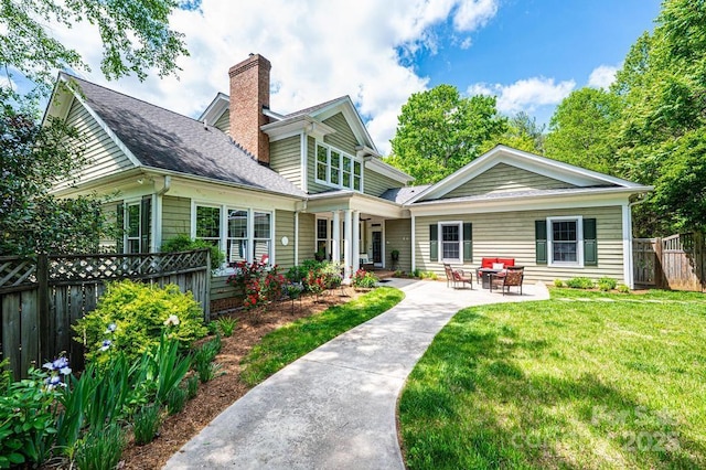 rear view of property with fence, a shingled roof, a chimney, a patio, and a yard