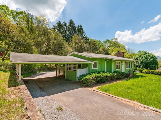 single story home featuring an attached carport, a chimney, a front yard, and aphalt driveway